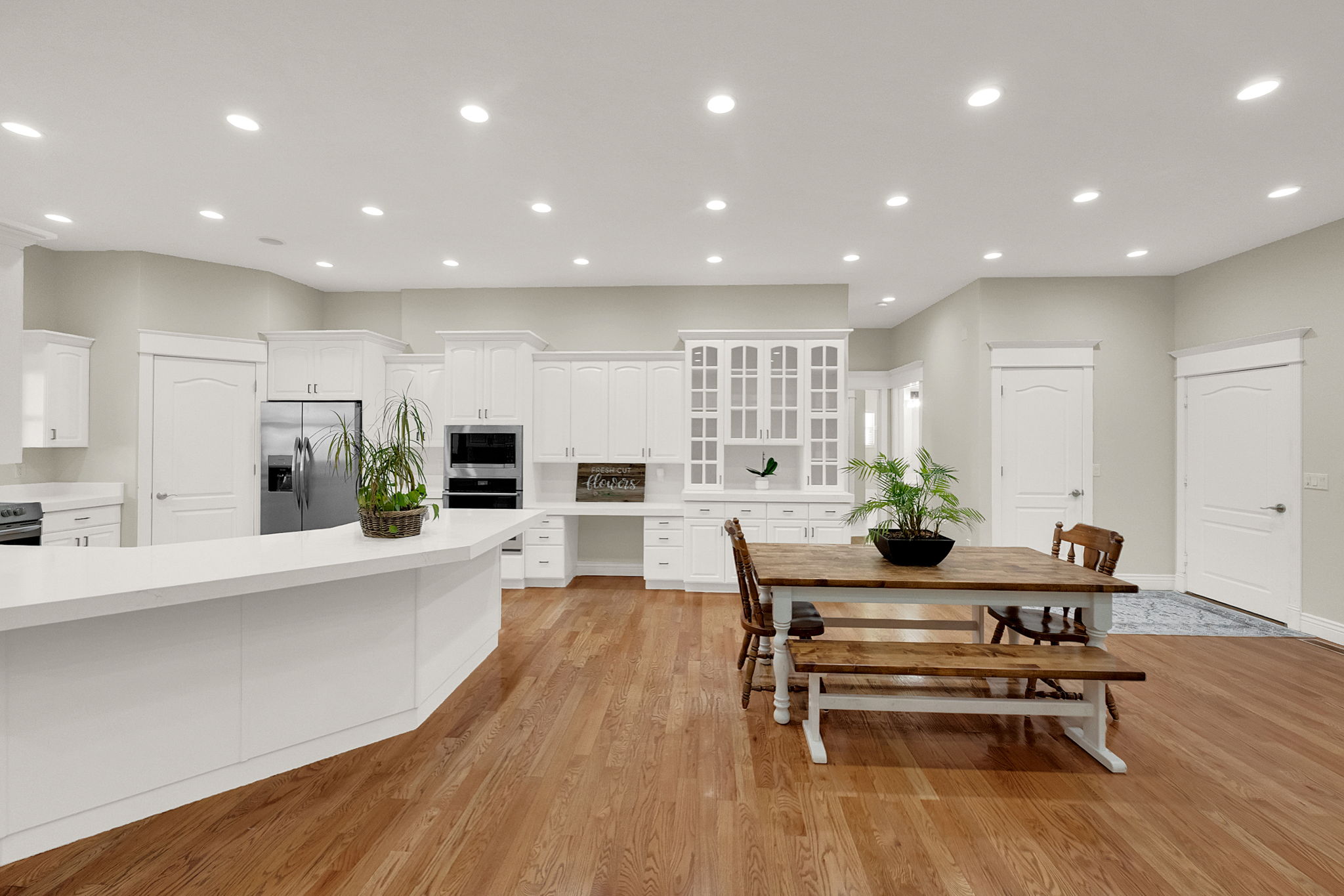 Open-concept kitchen and dining area featuring recessed lighting, extensive white cabinetry, built-in stainless steel appliances, a large kitchen island with a white countertop, and wood-finish flooring