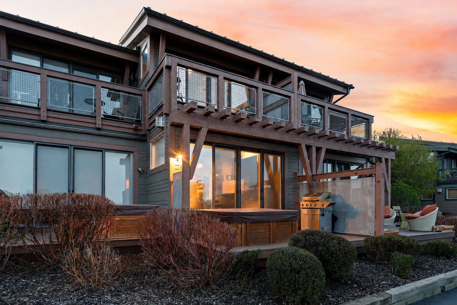 Multi-level exterior featuring a ground-level deck with a built-in hot tub, an overhead wooden pergola, and upper-level balconies with glass and metal railings