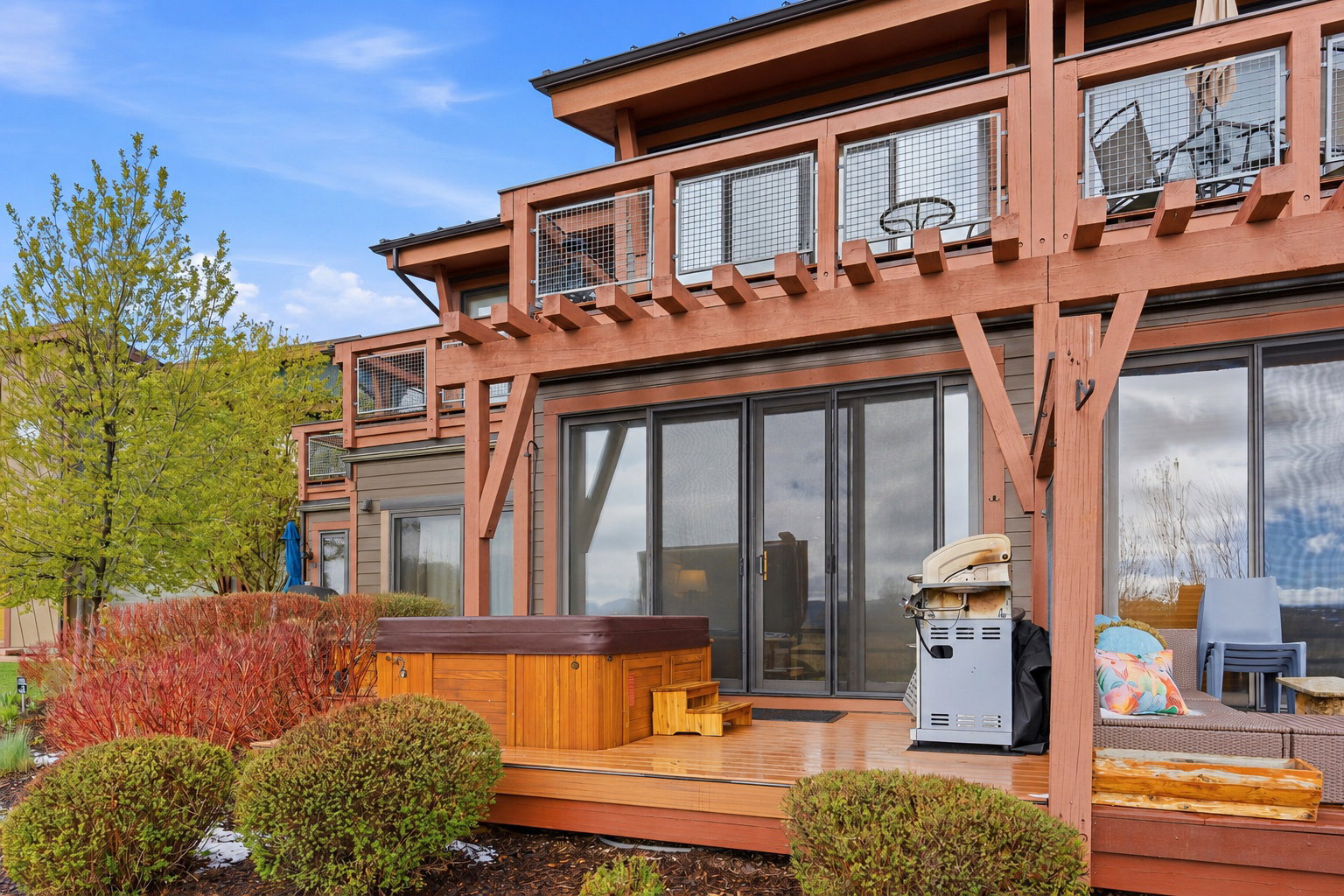 Expansive wood deck featuring a built-in hot tub with steps, multiple sliding glass doors, and a wood pergola