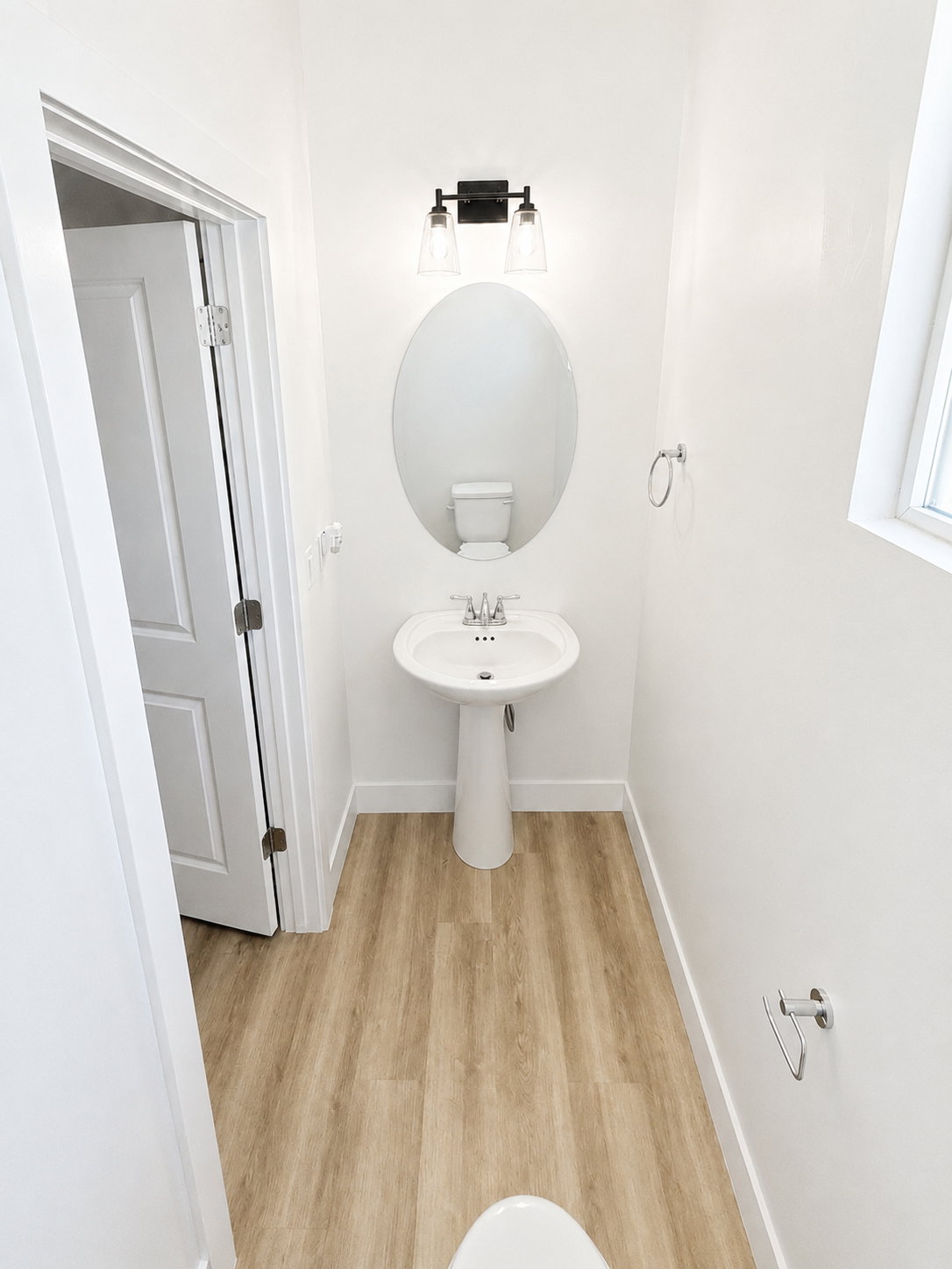 Powder room featuring wood-finish flooring, a white pedestal sink with a chrome faucet, and an oval mirror