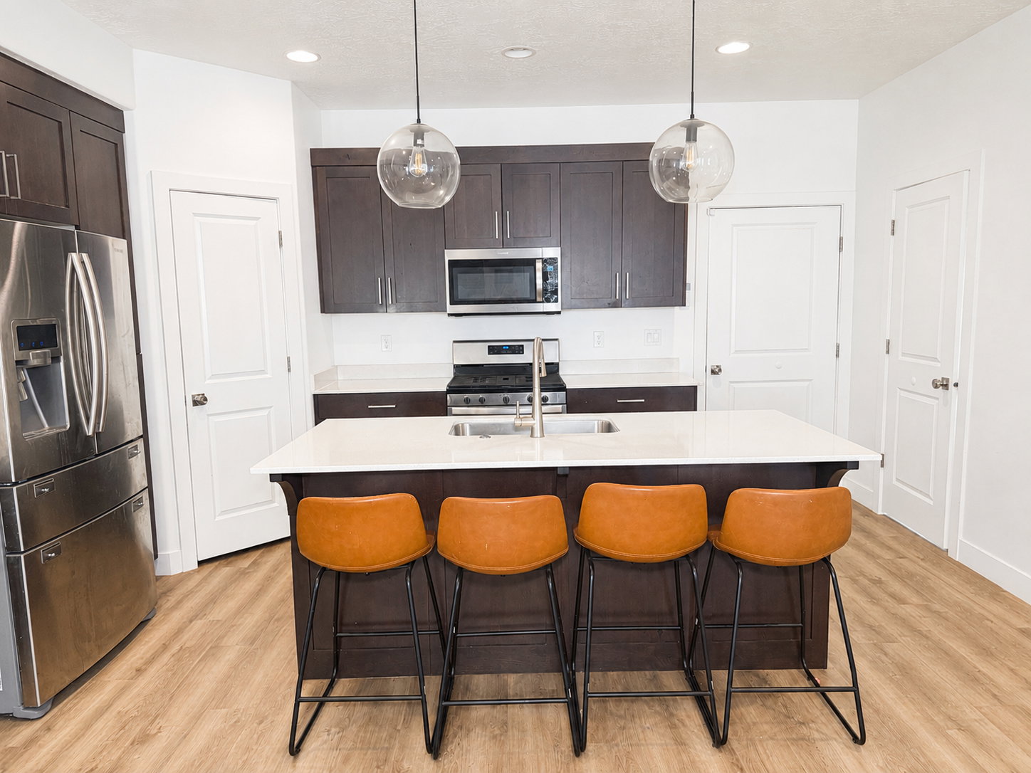 Kitchen featuring a central island with white countertop, dark wood-finish cabinetry, stainless steel appliances, and wood-finish flooring