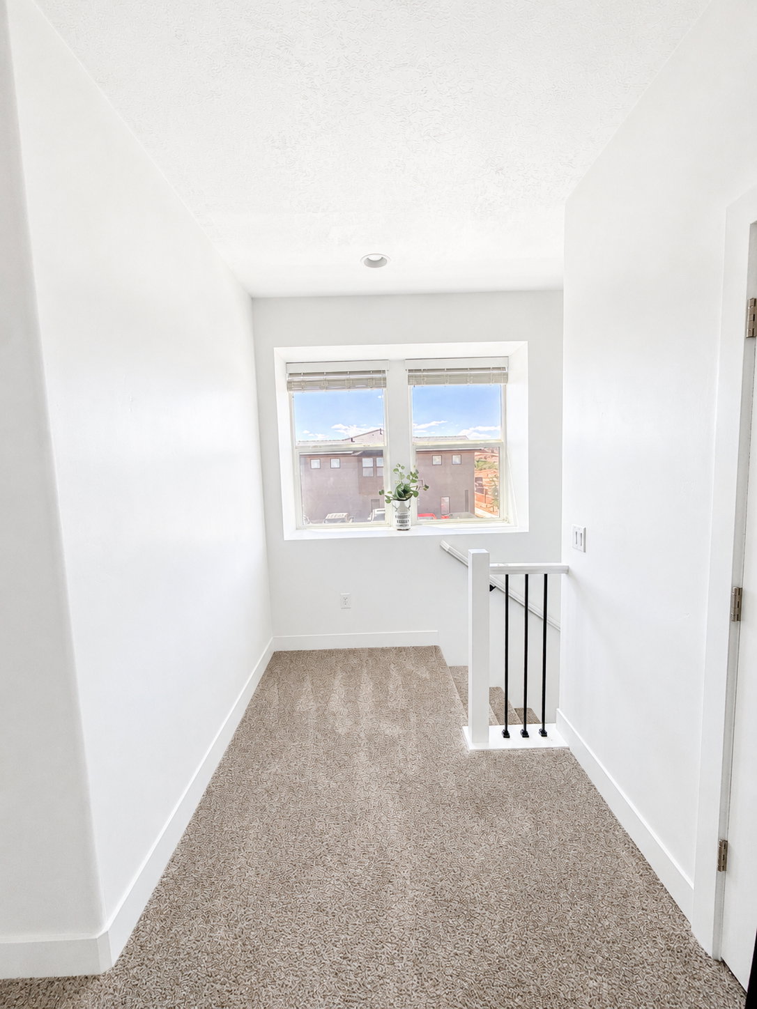 Carpeted hallway featuring a large window, white trim, and a white and black spindle railing