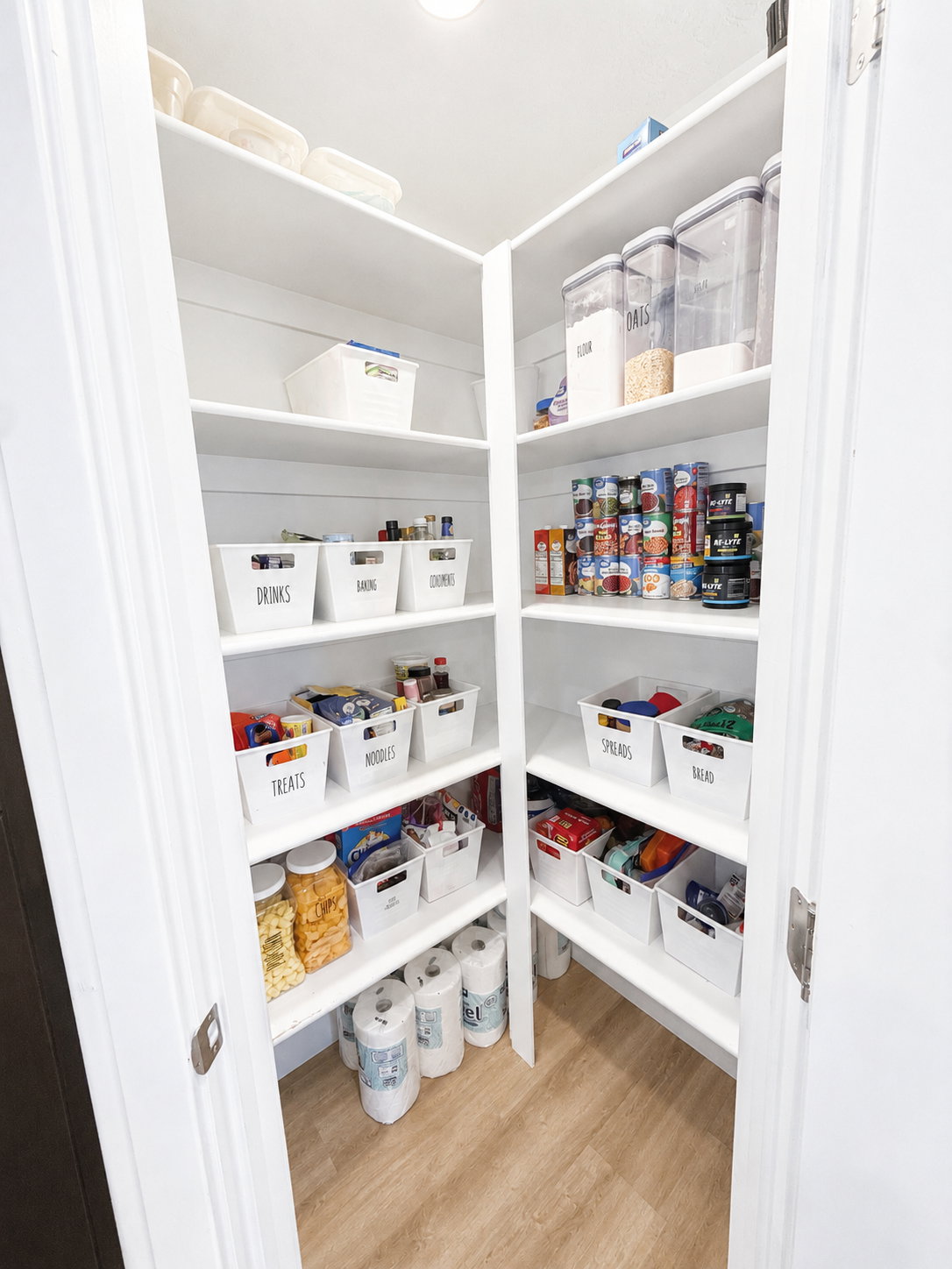 Corner pantry featuring multiple white built-in shelves and wood-finish flooring
