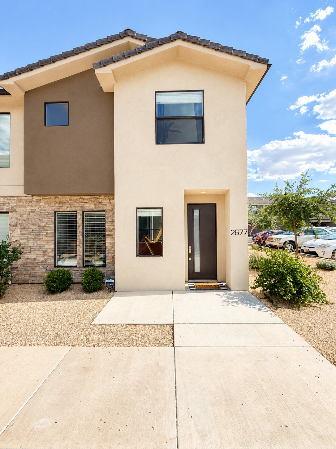 Contemporary stucco exterior featuring a dark brown entry door, contrasting stone veneer accents, and dark frame windows