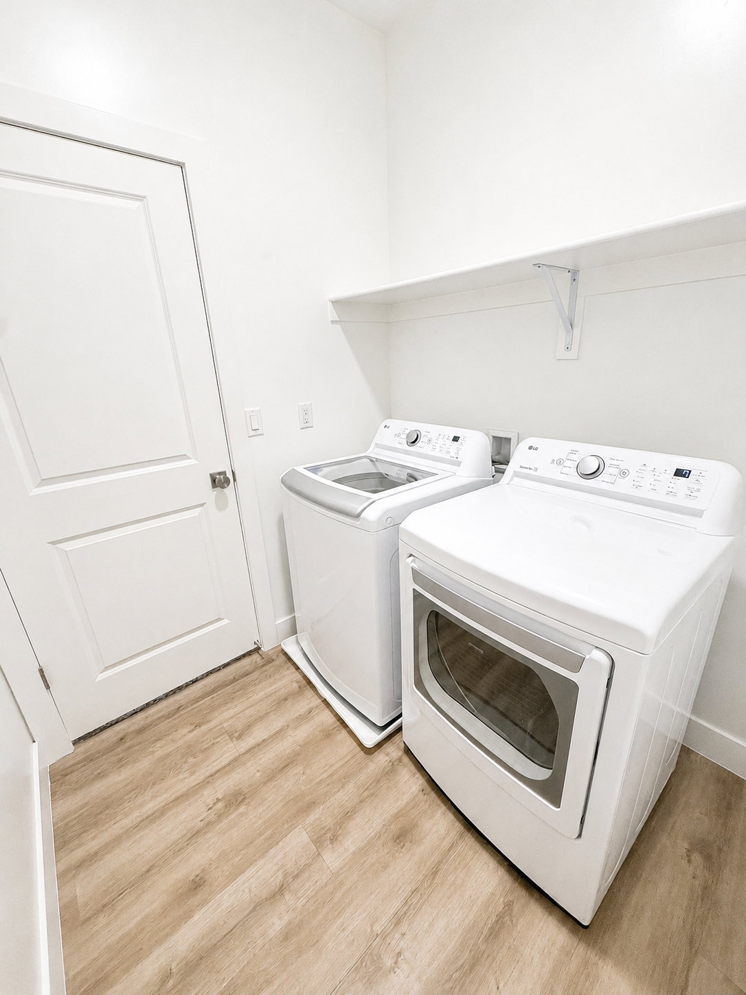 Dedicated laundry area featuring a washer and dryer, wood-finish flooring, and a white wall-mounted shelf