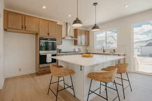 Contemporary kitchen featuring a substantial island with seating, pendant lighting, stainless steel double oven, light wood-finish cabinetry, and a tile backsplash