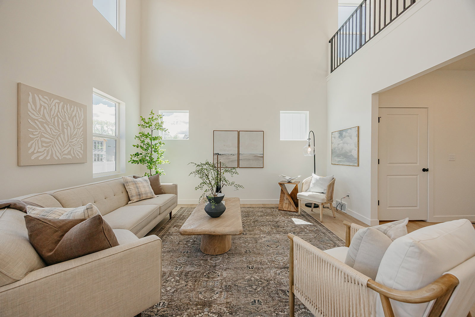 Double-height ceiling living room featuring abundant natural light, light wood-finish flooring, and a second-story interior balcony with a black metal railing