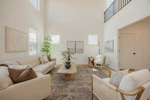 Double-height ceiling living room featuring abundant natural light, light wood-finish flooring, and a second-story interior balcony with a black metal railing