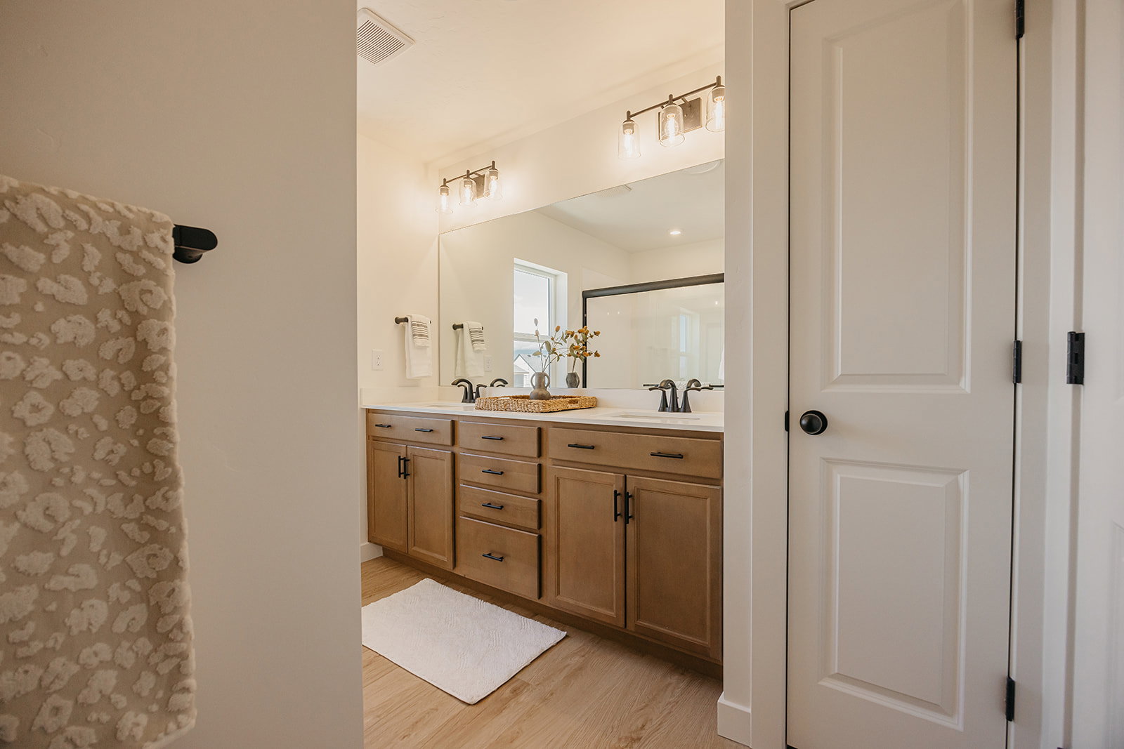 Double vanity featuring wood-finish cabinetry, black hardware, and an expansive mirror