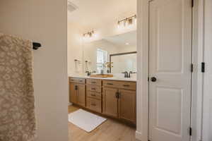 Double vanity featuring wood-finish cabinetry, black hardware, and an expansive mirror