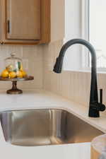 Kitchen sink featuring a matte black gooseneck faucet with pull-down sprayer, a stainless steel undermount basin, and white solid surface countertops