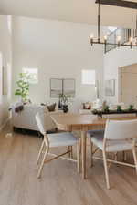 Spacious living area featuring high ceilings, wood-finish flooring, multiple windows, an open staircase with a black metal railing, and an exposed beam chandelier