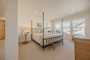 Spacious bedroom featuring light-toned carpeting, ample natural light from three large windows, recessed ceiling lighting, and a neutral wall palette