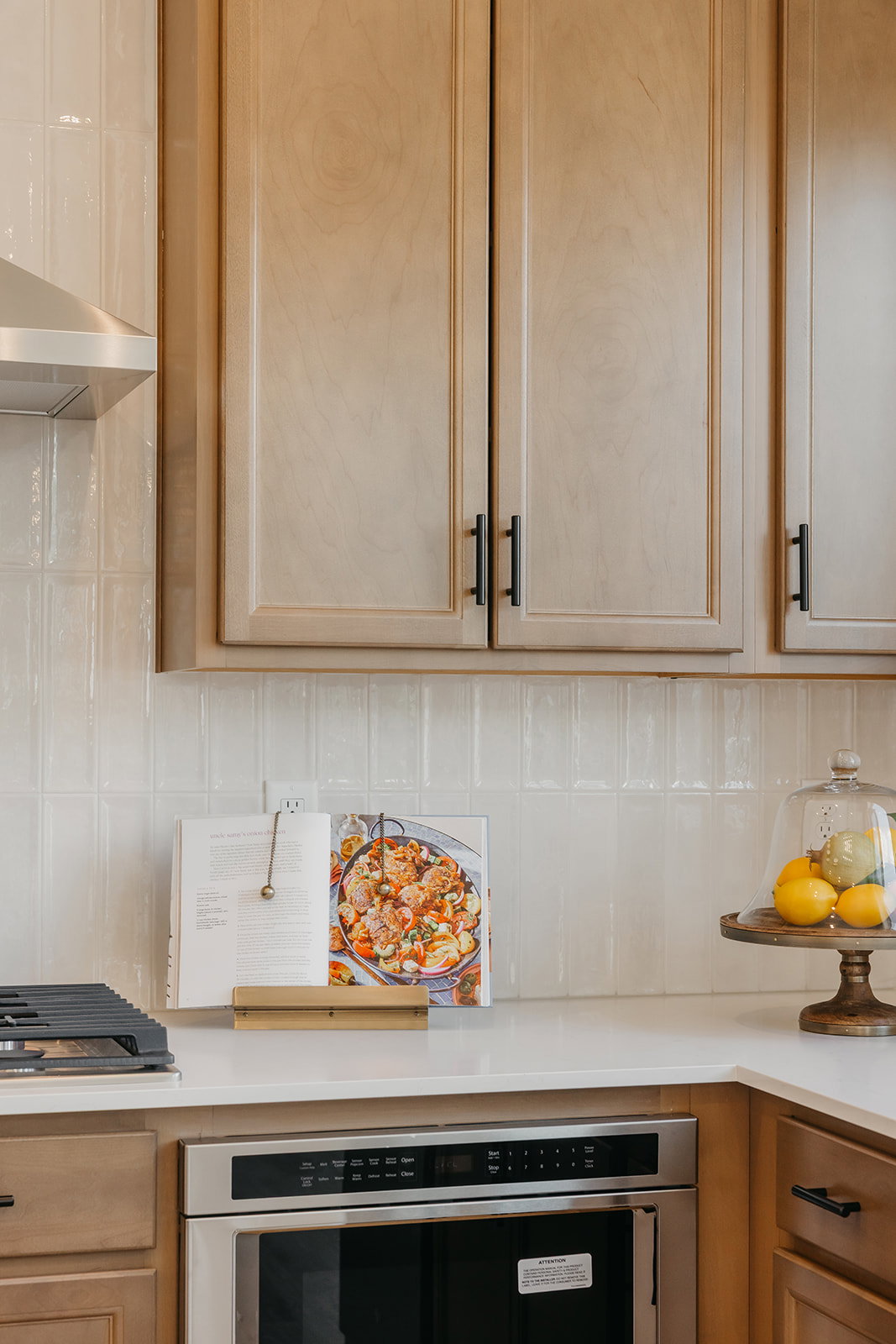 Kitchen featuring light wood-finish cabinetry with black hardware, white subway tile backsplash, and light-toned countertops