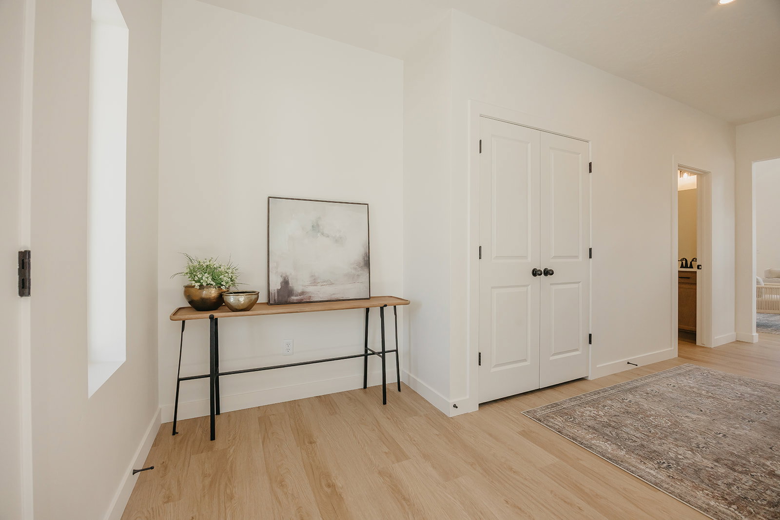 Bright hallway featuring wood-finish flooring, white baseboards, and a tall, narrow window