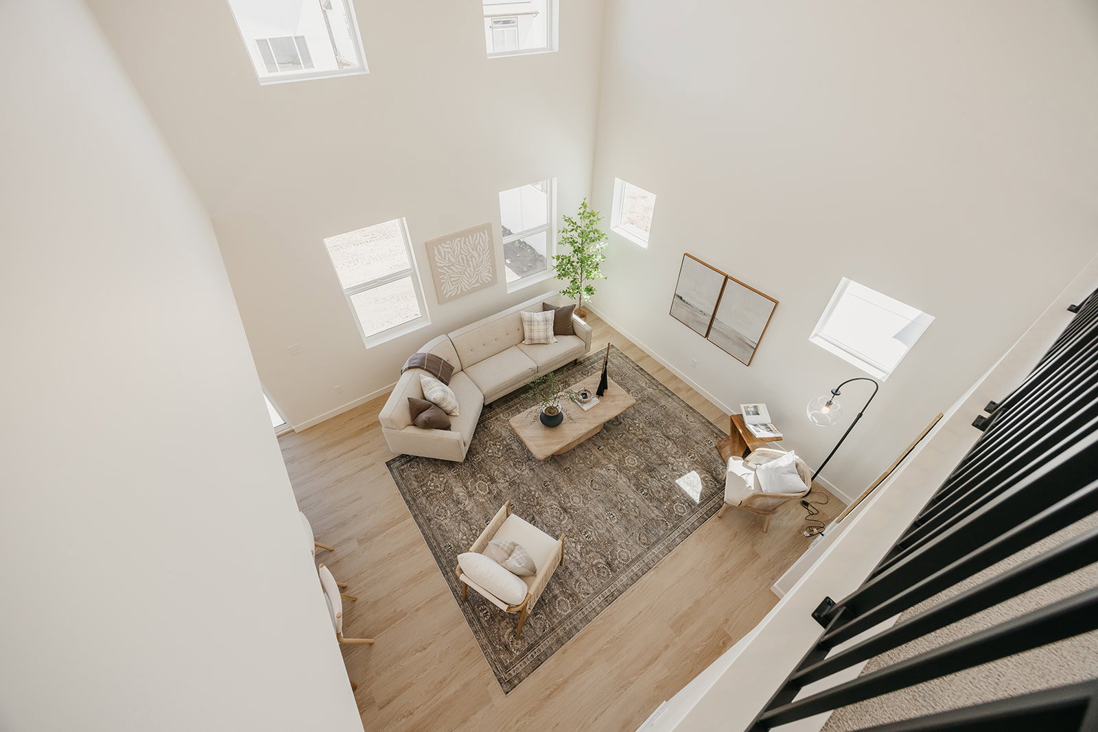 Two-story living area with high ceilings, multiple windows, light wood-finish flooring, and black metal staircase railing