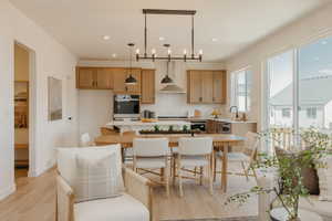 Open-concept living area featuring wood-finish flooring, a contemporary kitchen with light wood cabinetry and light countertops, and a dining space with a linear chandelier