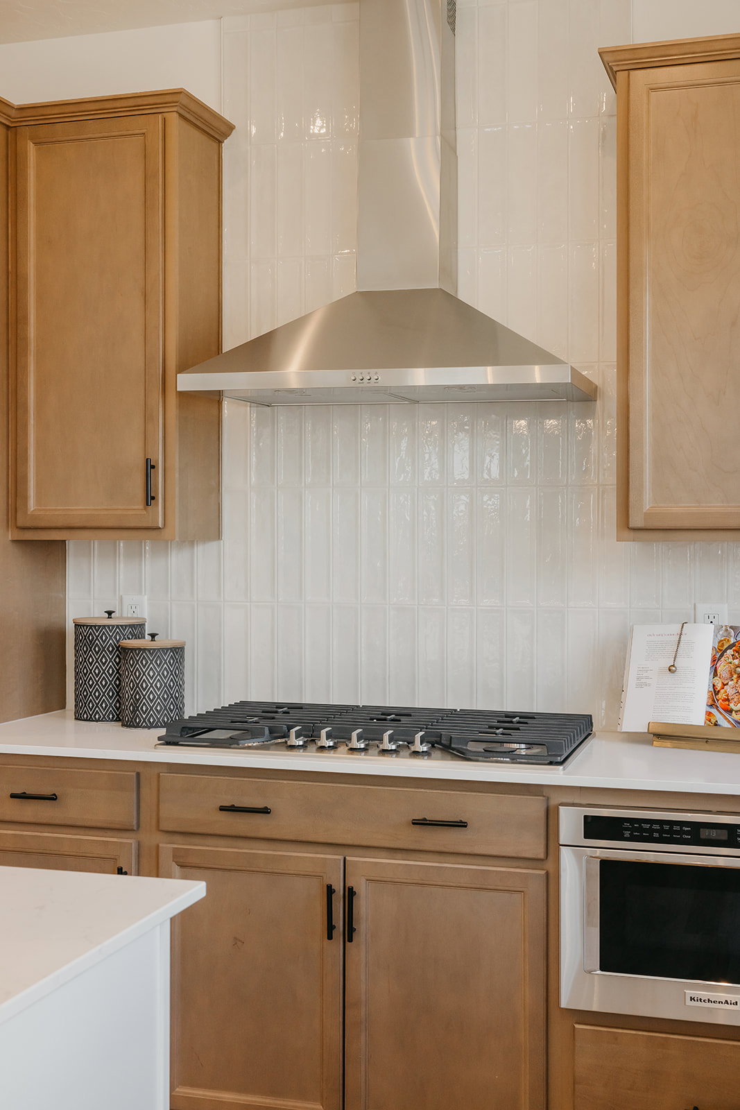 Kitchen featuring a stainless steel range hood, a cooktop with multiple burners, light-toned cabinetry, light countertops, and a built-in microwave