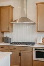Kitchen featuring a stainless steel range hood, a cooktop with multiple burners, light-toned cabinetry, light countertops, and a built-in microwave