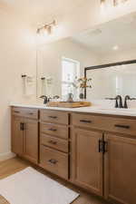 Dual vanity with light wood-finish cabinetry, black hardware, and white countertops