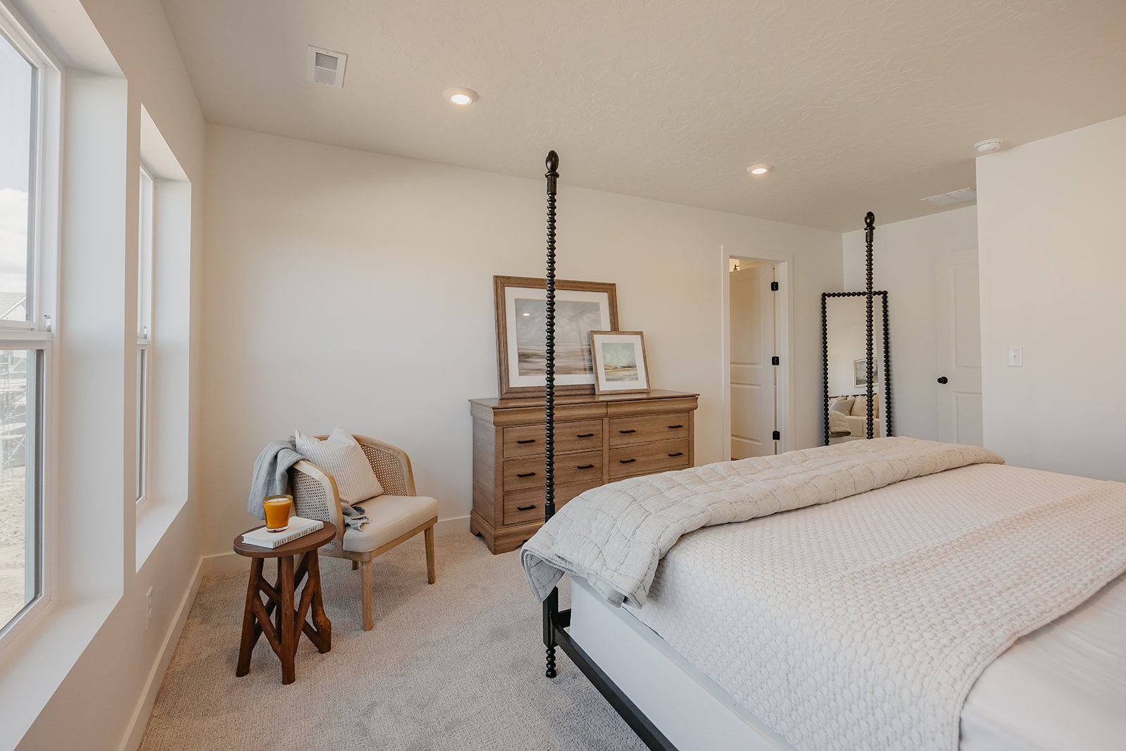 Spacious bedroom with light beige wall paint, two large vertical windows, recessed ceiling lighting, and light gray carpet flooring