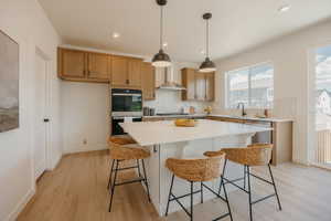 Contemporary kitchen featuring a large central island with solid surface countertop, wood-finish flooring, built-in double ovens, and stainless steel appliances