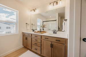 Double vanity with light wood-finish cabinetry, white countertops, dual sinks, and matte black fixtures