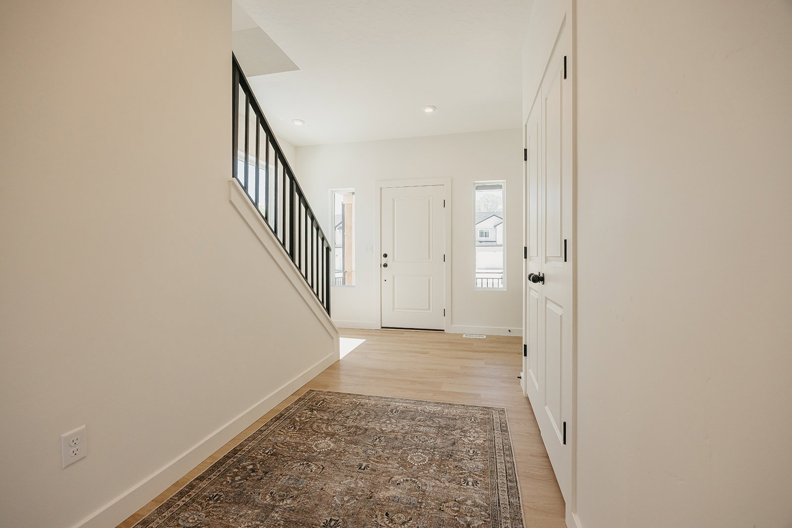 Entryway featuring light wood-finish flooring, white paneled doors, and a staircase with a black metal railing