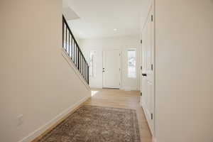 Entryway featuring light wood-finish flooring, white paneled doors, and a staircase with a black metal railing