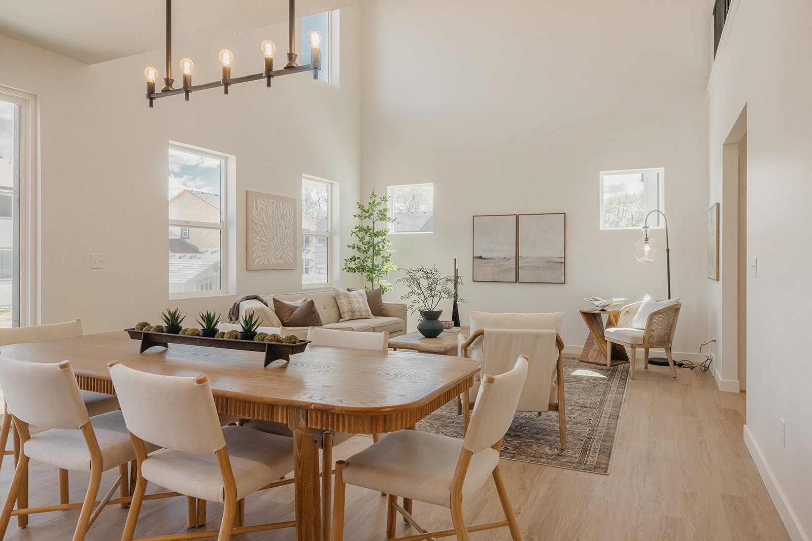 Open-concept living area with vaulted ceilings, a linear chandelier, multiple windows, and wood-finish flooring throughout