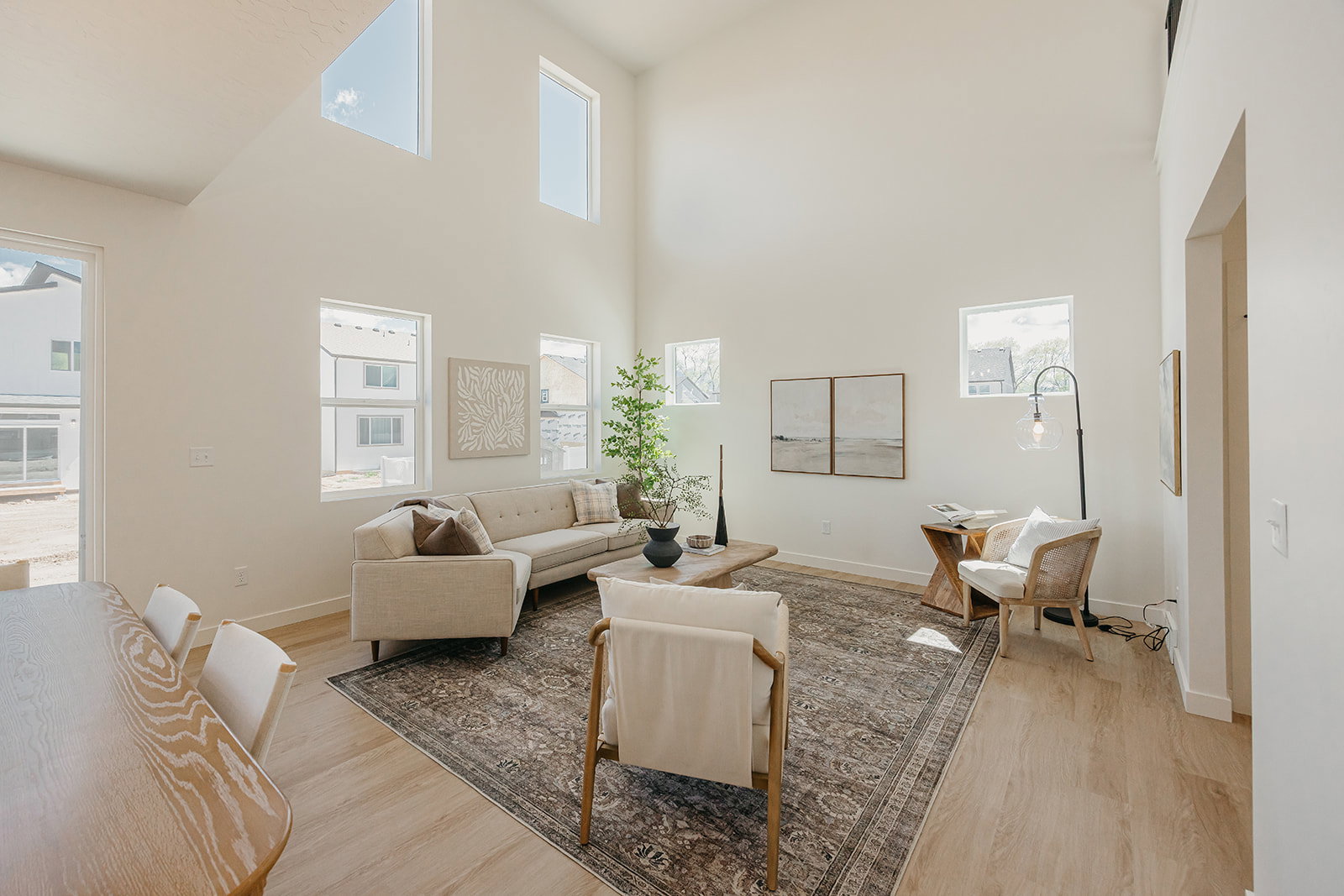 Vaulted ceilings defining a spacious living area, featuring light wood-finish flooring, multiple windows providing ambient illumination, and a neutral color palette