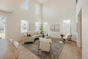Vaulted ceilings defining a spacious living area, featuring light wood-finish flooring, multiple windows providing ambient illumination, and a neutral color palette