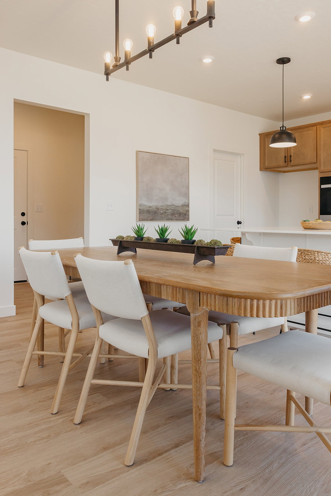 Open-concept dining area featuring wood-finish flooring, a linear chandelier, recessed lighting, and a kitchen island with pendant lighting