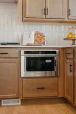 Built-in stainless steel microwave oven integrated into natural wood-finish cabinetry with black hardware