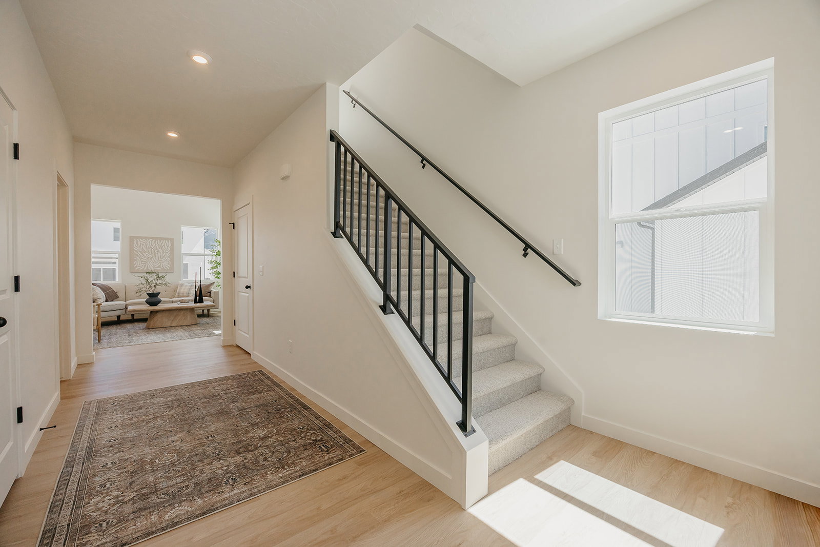 Entryway featuring light wood-finish flooring, a staircase with carpeting, and a black iron railing
