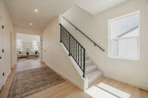 Entryway featuring light wood-finish flooring, a staircase with carpeting, and a black iron railing
