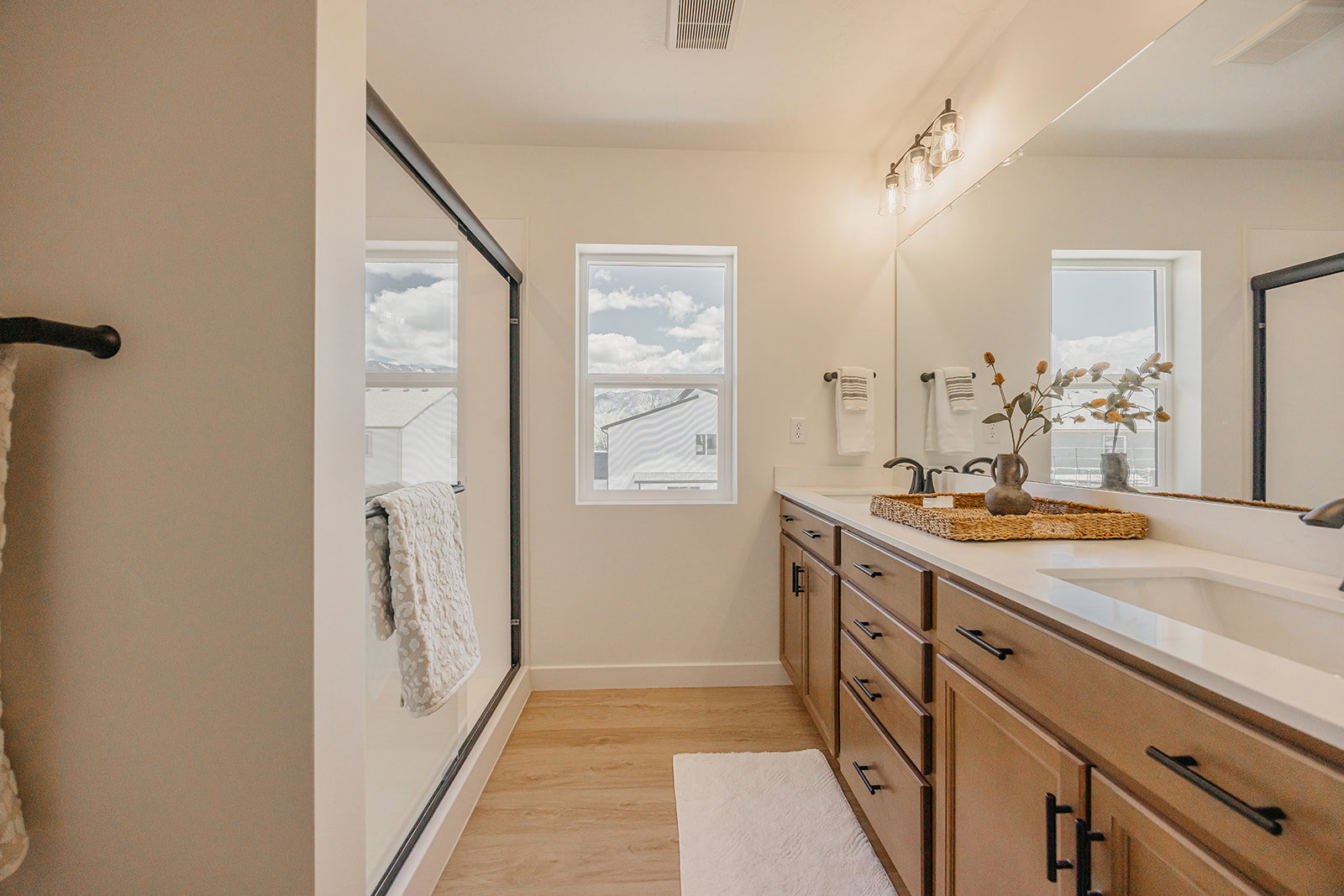 Bathroom featuring a double vanity with light wood-finish cabinetry, white countertops, and black hardware