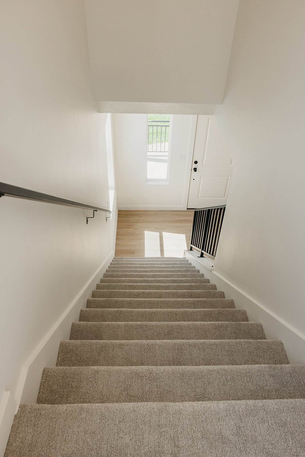 Carpeted staircase with contrasting black metal handrail and balusters, leading to a bright landing with wood-finish flooring