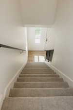 Carpeted staircase with contrasting black metal handrail and balusters, leading to a bright landing with wood-finish flooring
