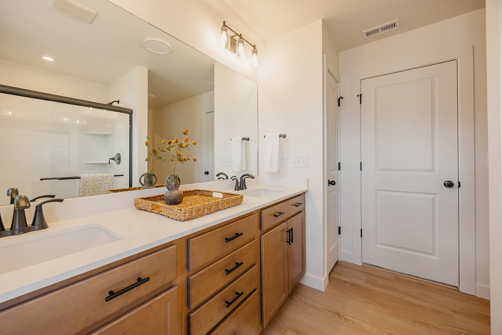Dual vanity with integrated sinks, white countertops, wood-finish cabinetry, and black hardware