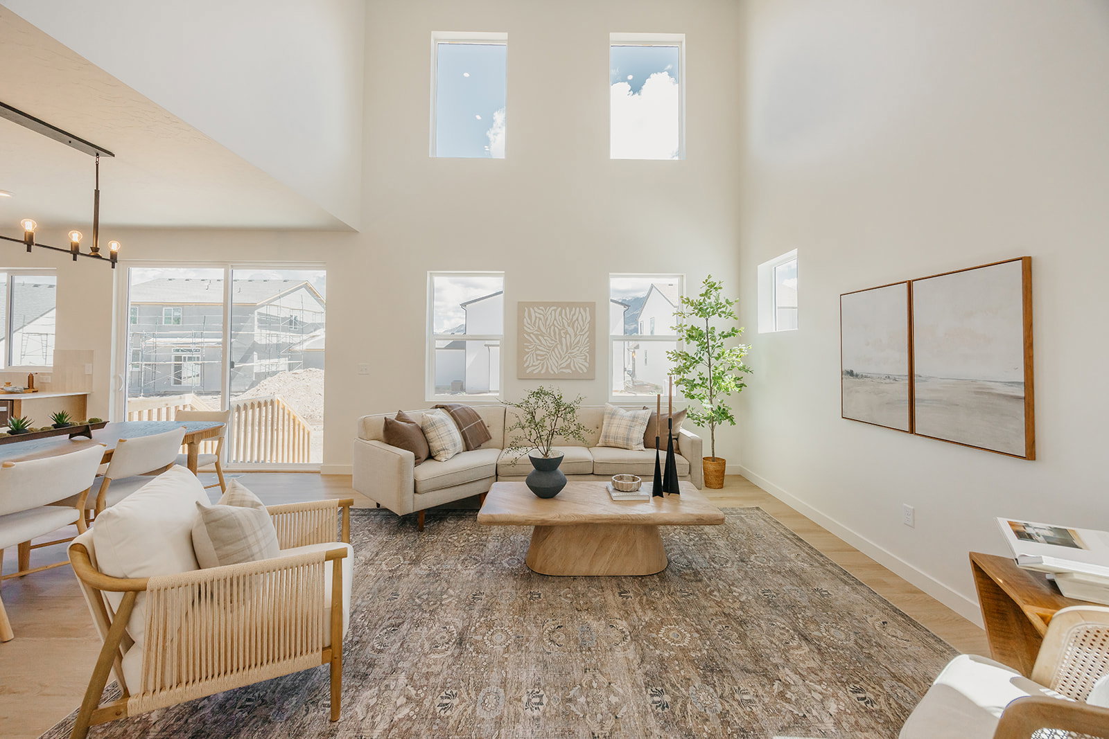 Two-story living area featuring a vaulted ceiling, light-toned wood-finish flooring, multiple windows, and a black linear chandelier
