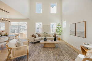 Two-story living area featuring a vaulted ceiling, light-toned wood-finish flooring, multiple windows, and a black linear chandelier