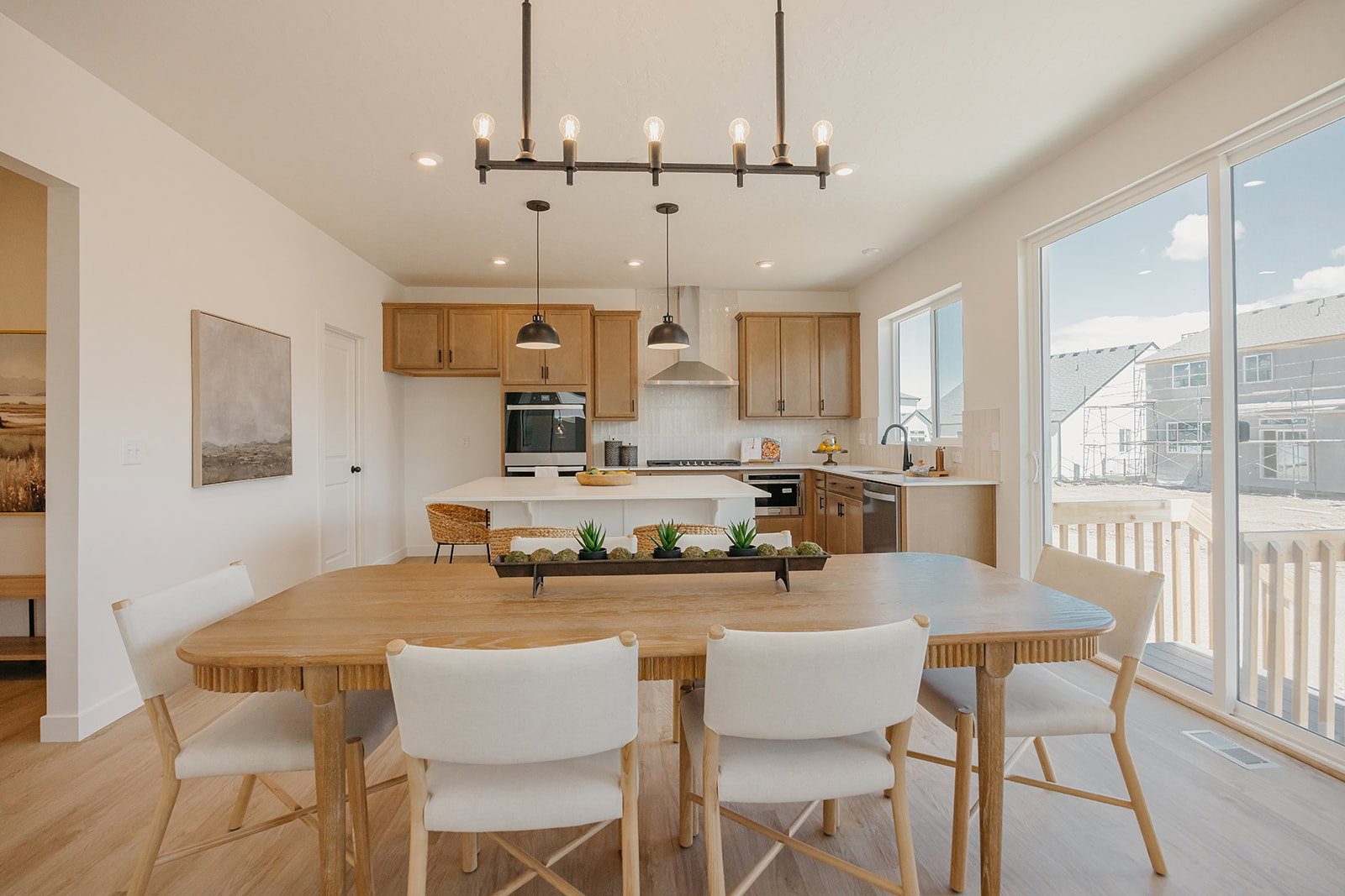 Open-concept dining area with wood-finish flooring, featuring a contemporary chandelier, recessed lighting, and a sliding glass door providing access to an outdoor deck
