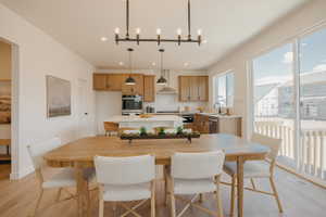 Open-concept dining area with wood-finish flooring, featuring a contemporary chandelier, recessed lighting, and a sliding glass door providing access to an outdoor deck