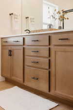 Warm wood-finish cabinetry featuring black hardware, a light-colored countertop, and a large mirror