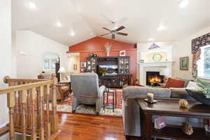 Living area featuring vaulted ceilings, wood-finish flooring, a fireplace with a white mantel, recessed lighting, and a ceiling fan