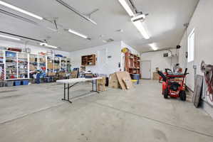Spacious garage featuring a concrete floor, built-in shelving, ample overhead lighting, multiple windows, and a dedicated utility door