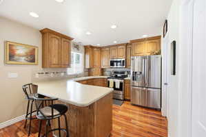 Kitchen featuring wood cabinetry, stainless steel appliances, a light-toned countertop, tile backsplash, and wood-finish flooring