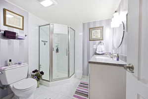 Full bathroom featuring a corner shower with glass enclosure, white vanity with stone countertop, oval vanity mirror, and white toilet