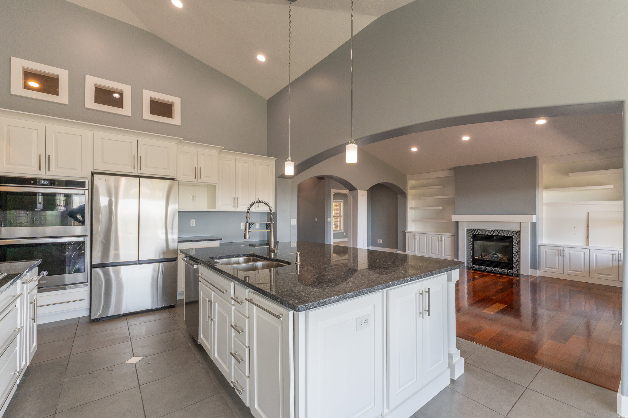 Spacious kitchen featuring an expansive center island with a double basin sink and dark stone countertop, white cabinetry with brushed nickel hardware, stainless steel appliances, and tile flooring